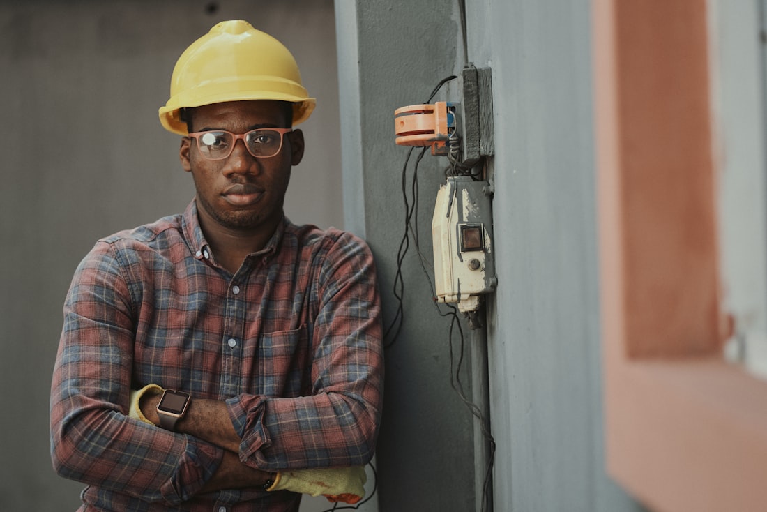 A professional inspector in safety gear beside an exterior electrical service panel
